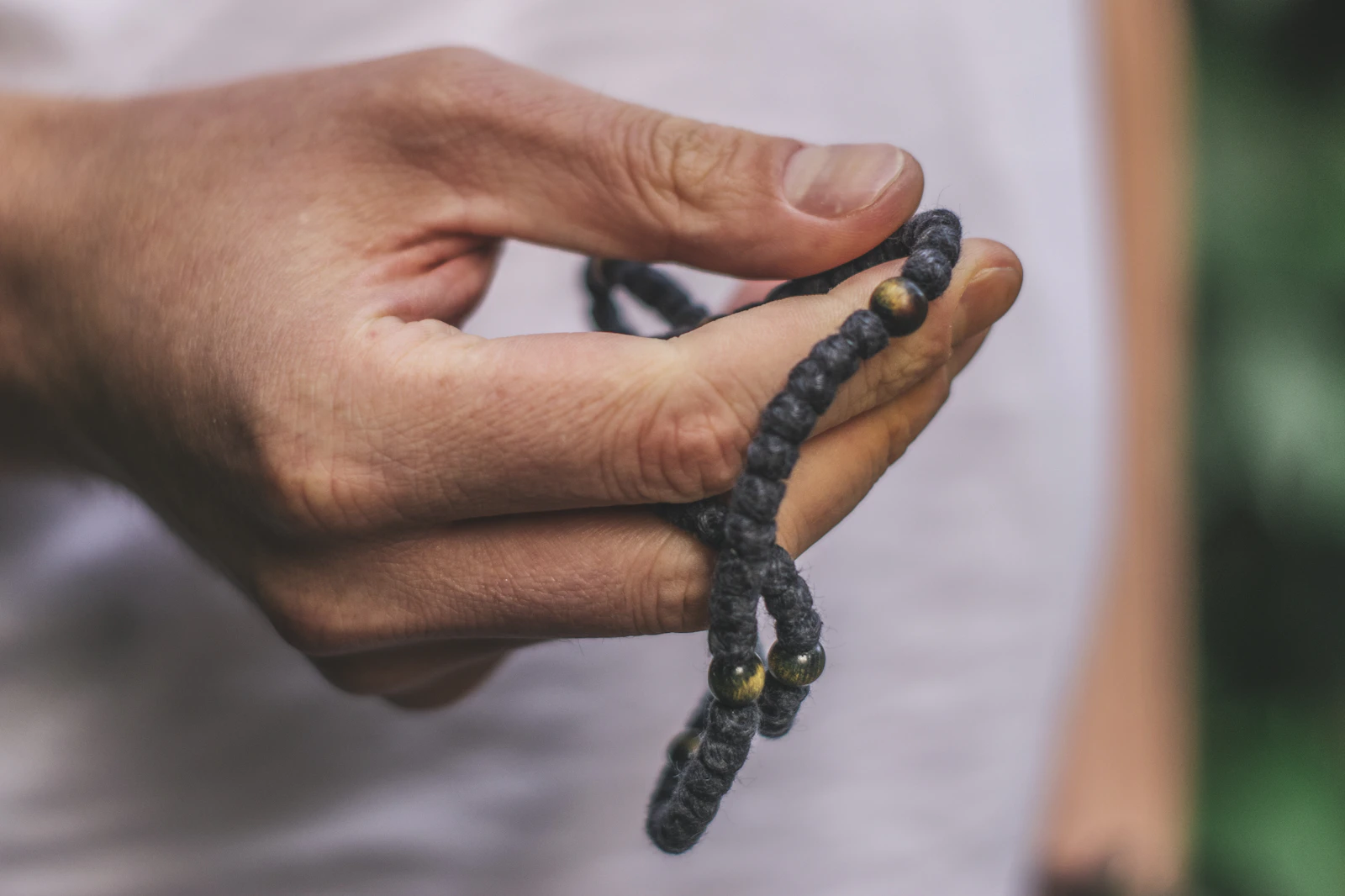 A hand holding a dark knotted prayer cord with small gold-coloured spacer beads